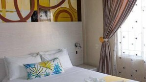 Habitación de hotel con una cama grande, una mesita de noche, una pared con arte abstracto y una ventana con cortinas.