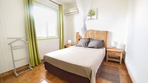 Ein Schlafzimmer mit Bett, Nachttischen, einer Hängelampe, einem Fenster mit Vorhängen und einem Heizkörper.