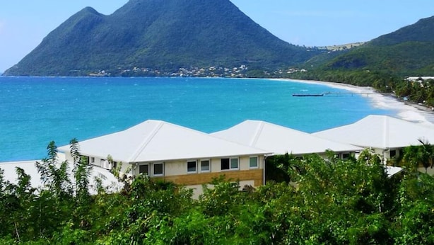 Ein Küstenhotel mit weißen Zelten, einem Strand und einem Berg im Hintergrund.