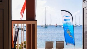 Blick vom Balkon auf einen Yachthafen mit Segelbooten, einer roten Flagge und einem blauen Banner mit Schrift.