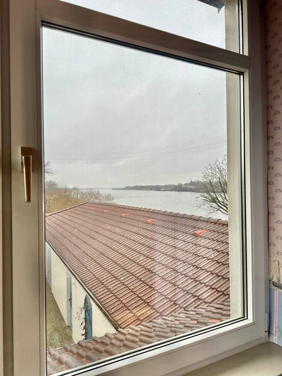 A window with a view of a building's roof and a body of water.