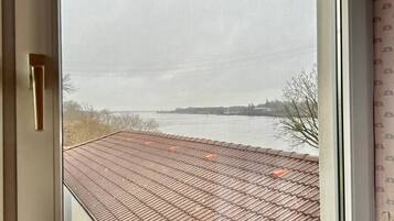 A window with a view of a building's roof and a body of water.
