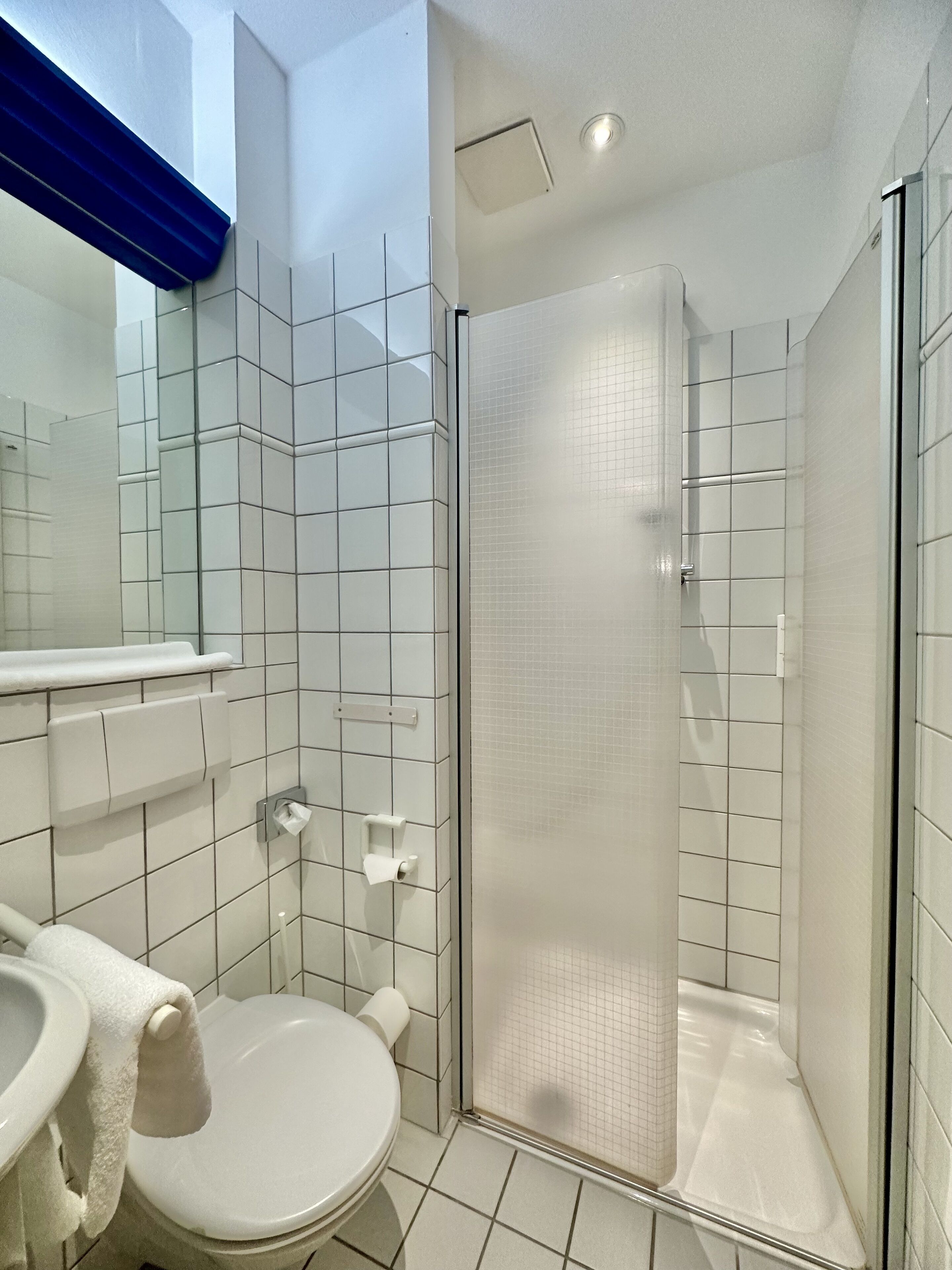Une salle de bain moderne avec une douche à parois de verre, des carreaux blancs et un porte-rouleau de papier toilette visible.
