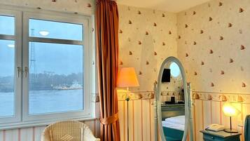 A hotel room with a bed, a chair, a desk, a mirror, and a window overlooking a body of water.