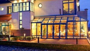 A modern two-story house with a glass conservatory, a well-lit entrance, and a landscaped front yard. - Gästehaus Weserblick (Berne)