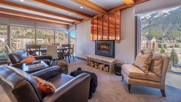 A modern living room with a fireplace, leather sofas, and a large window offering a mountain view. - Snowflake on Copper Mountain 3 Bedroom Ski In / Ski Out! (Frisco)
