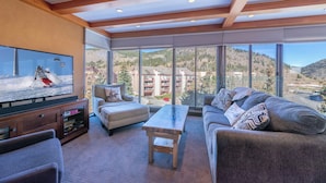 A modern living room with a large TV, comfortable seating, and a view of a mountainous landscape. - Snowflake on Copper Mountain 3 Bedroom Ski In / Ski Out! (Frisco)