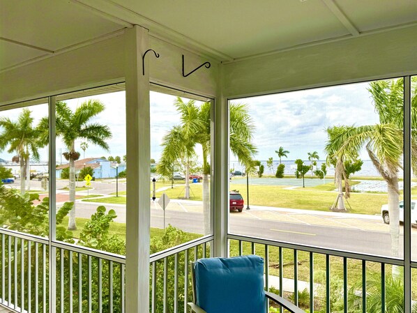 A covered outdoor area with a view of a road, palm trees, and a body of water. - “Sailboats & Sunsets” Unforgettable Harbor Views - Heart of Historic Downtown (Punta Gorda)