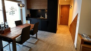 Une cuisine moderne avec des meubles de rangement aux couleurs sombres, une table à manger en bois et un luminaire suspendu.