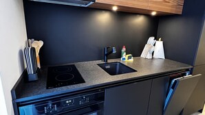 Une cuisine moderne avec des meubles en bois, un plan de travail noir, un four encastré et un lave-vaisselle.