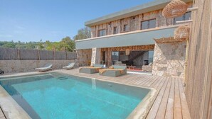 A modern house with a swimming pool, outdoor seating, and a stone wall.