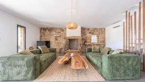 A modern living room with a stone wall, green upholstered sofas, a central coffee table, and a hanging light fixture.