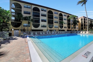 A hotel with a pool area, featuring a large rectangular pool, lounge chairs, and palm trees.