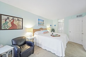 A hotel room with a bed, a chair, a table, and artwork on the walls.