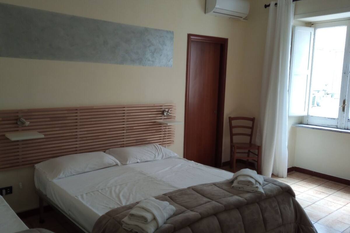 A bedroom with a wooden headboard, a bed with white linens, a chair, and a window with curtains.