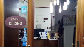 A hotel reception area with a wooden reception desk, a digital display, and a staircase in the background. - Hotel Eliseo Napoli (Naples)