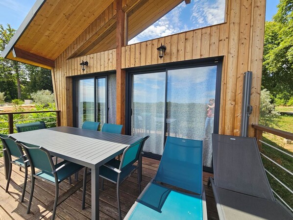 A wooden deck with a table and chairs, large sliding glass doors, and a view of the outdoors. - Cabane Avec vue Exceptionnelle à Dole (Dole)