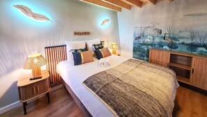 Quarto com cama grande, luminárias de cabeceira, pintura de pássaros e teto de madeira.