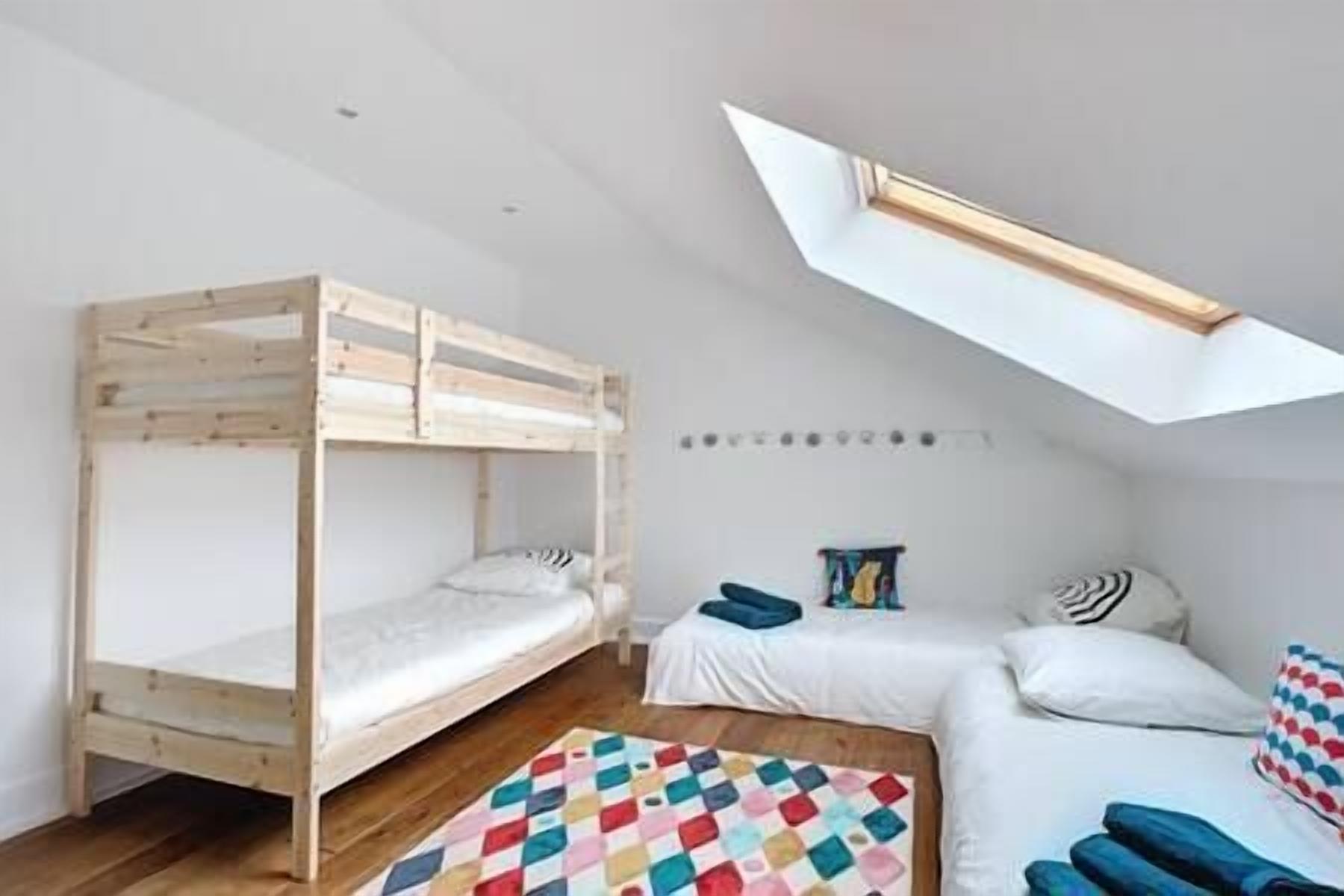 Une chambre avec un lit superposé, un lit simple et un tapis coloré.