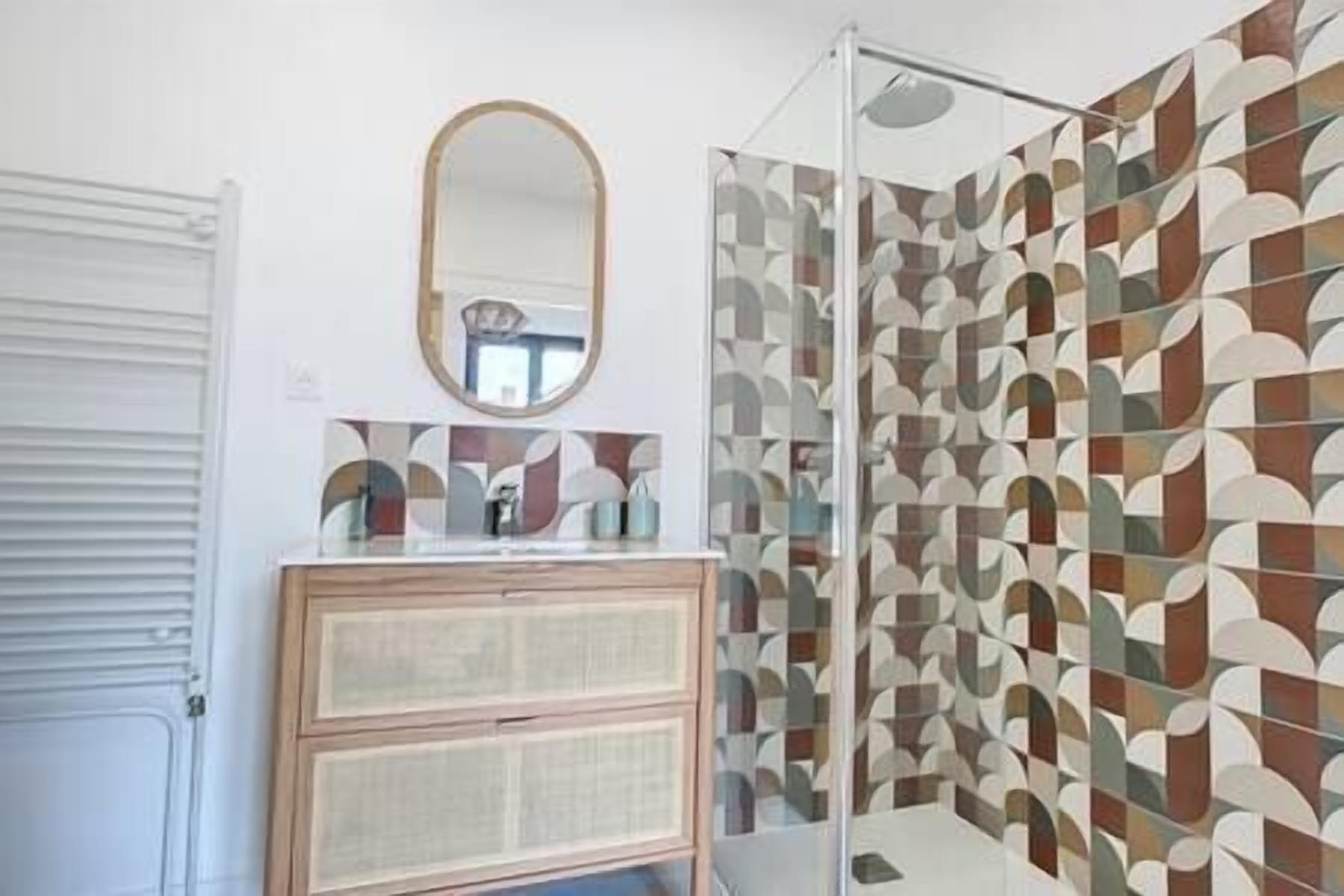 A bathroom with a geometric patterned shower curtain, a wooden cabinet, and a mirror above it.