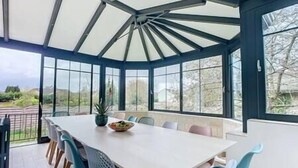 Une véranda dotée d’une grande table et de chaises, de larges fenêtres et offrant une vue sur l’extérieur.