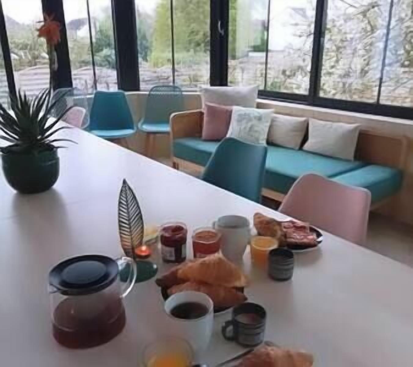 Een ontbijtsetting met een tafel, stoelen en een bank in een kamer met grote ramen.