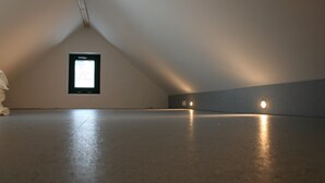 Una habitación ática vacía con techo inclinado, un ventanal pequeño y suelo de hormigón.