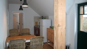 Una cocina compacta con refrigerador, microondas y armarios de madera. Una mesa de comedor con sillas de mimbre está ubicada frente a la cocina.