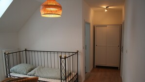 Un dormitorio con techo inclinado, estructura de cama metálica, una silla de mimbre y una lámpara colgante.