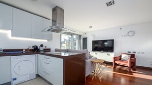 Una cocina moderna con lavavajillas integrado, una isla grande y una zona de comedor con televisor y asientos.