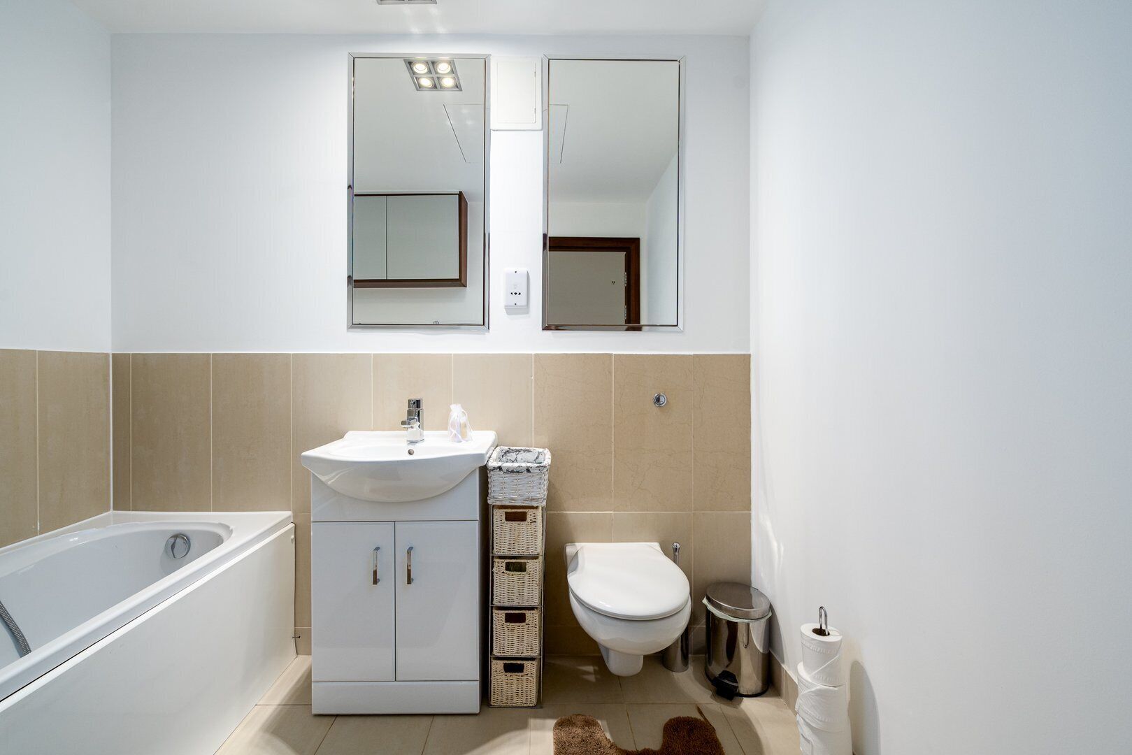 A modern bathroom with a white sink, a bathtub, a toilet, and a mirror above the sink.