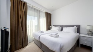 Habitación de hotel con una cama grande, dos mesitas de noche, un calentador y una ventana con cortinas.