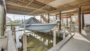 A boat docked under a wooden structure with a concrete floor, surrounded by wooden posts and a rope barrier. - Private Dock, Lanai: Bayou Retreat in Barataria! (Barataria)