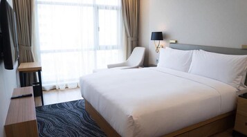 Una habitación de hotel con una cama grande, un escritorio, una silla, una lámpara y una ventana con cortinas.