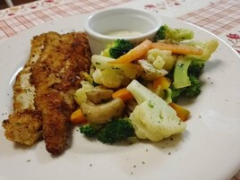 Un plato con una milanesa, verduras mixtas y un recipiente pequeño con salsa.