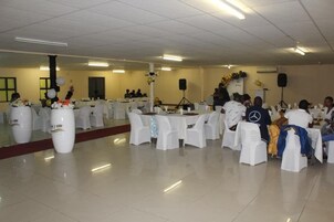 Un salón de banquetes con mesas redondas cubiertas con manteles blancos, sillas con fundas blancas y centros de mesa florales.