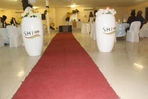 Vestíbulo de hotel con una alfombra roja que conduce a una zona de recepción, sillas blancas y dos grandes jarrones con el logotipo del hotel.