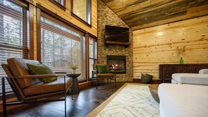 Una sala de estar acogedora con chimenea de piedra, paredes de madera y ventanas amplias.