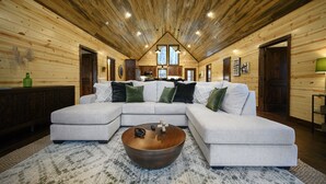 Un salón espacioso con un amplio sofá modular en forma de L, una mesa de centro de madera y un techo alto con vigas de madera.