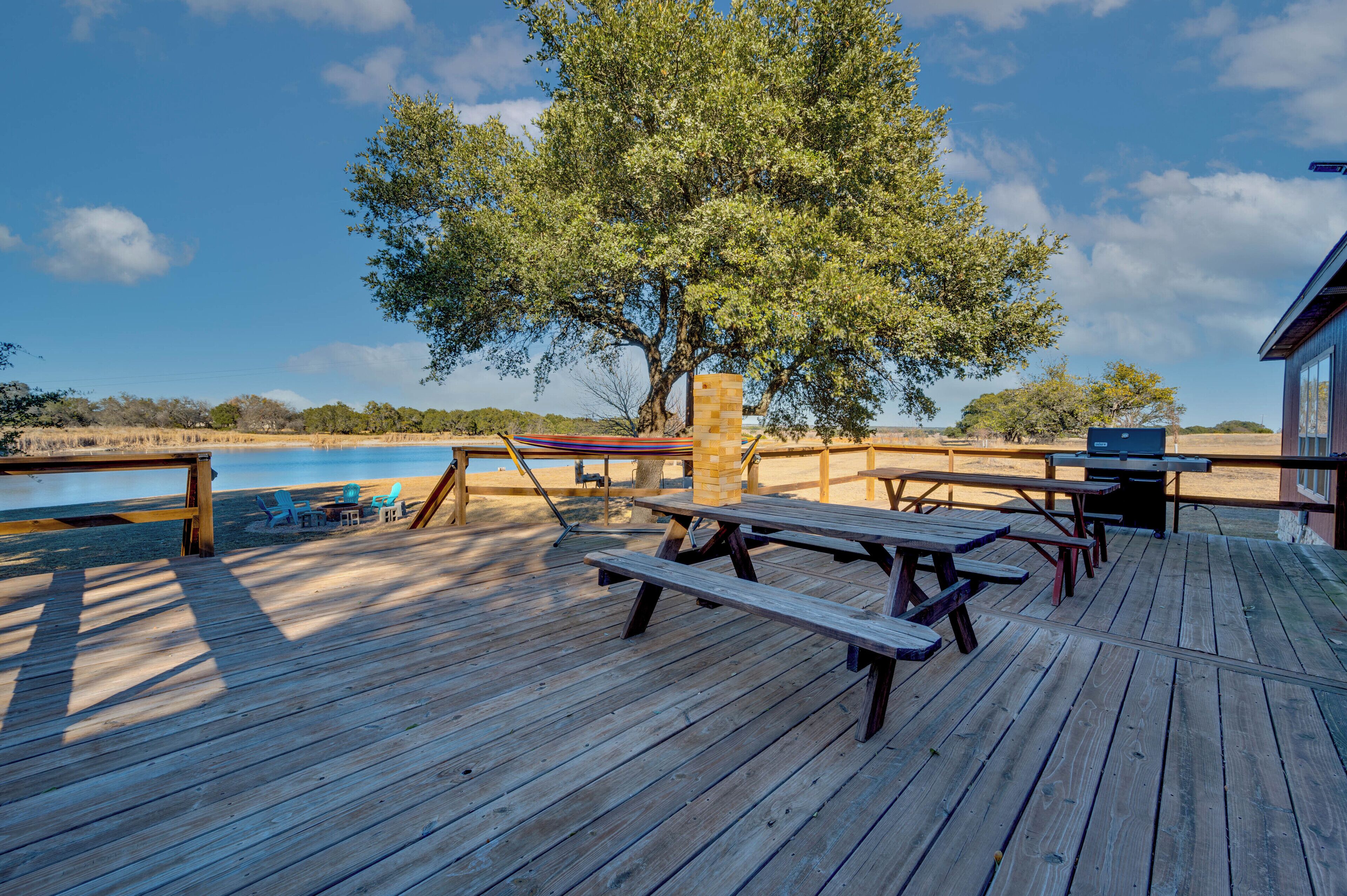 Eine Holzterrasse mit Picknicktischen und Liegestühlen mit Blick auf ein Gewässer.