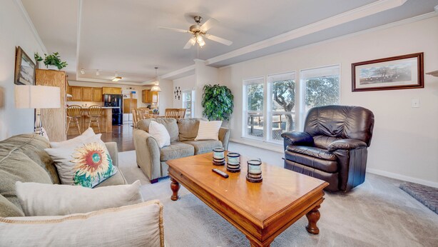 A spacious living room with a wooden coffee table, a leather armchair, and a sofa. A ceiling fan and a dining area are visible in the background.