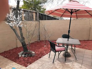 Ein Patio mit Tisch und Stühlen, einem gestreiften Sonnenschirm und einem Baum mit weißen Blüten.