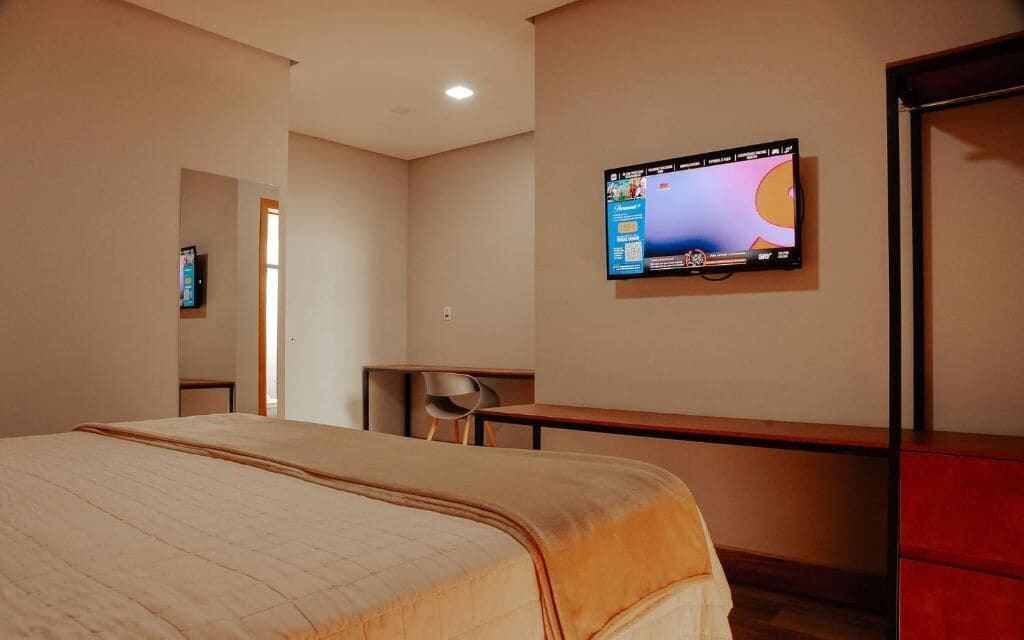 Et hotelværelse med en seng, et skrivebord, en stol og et fjernsyn på væggen.