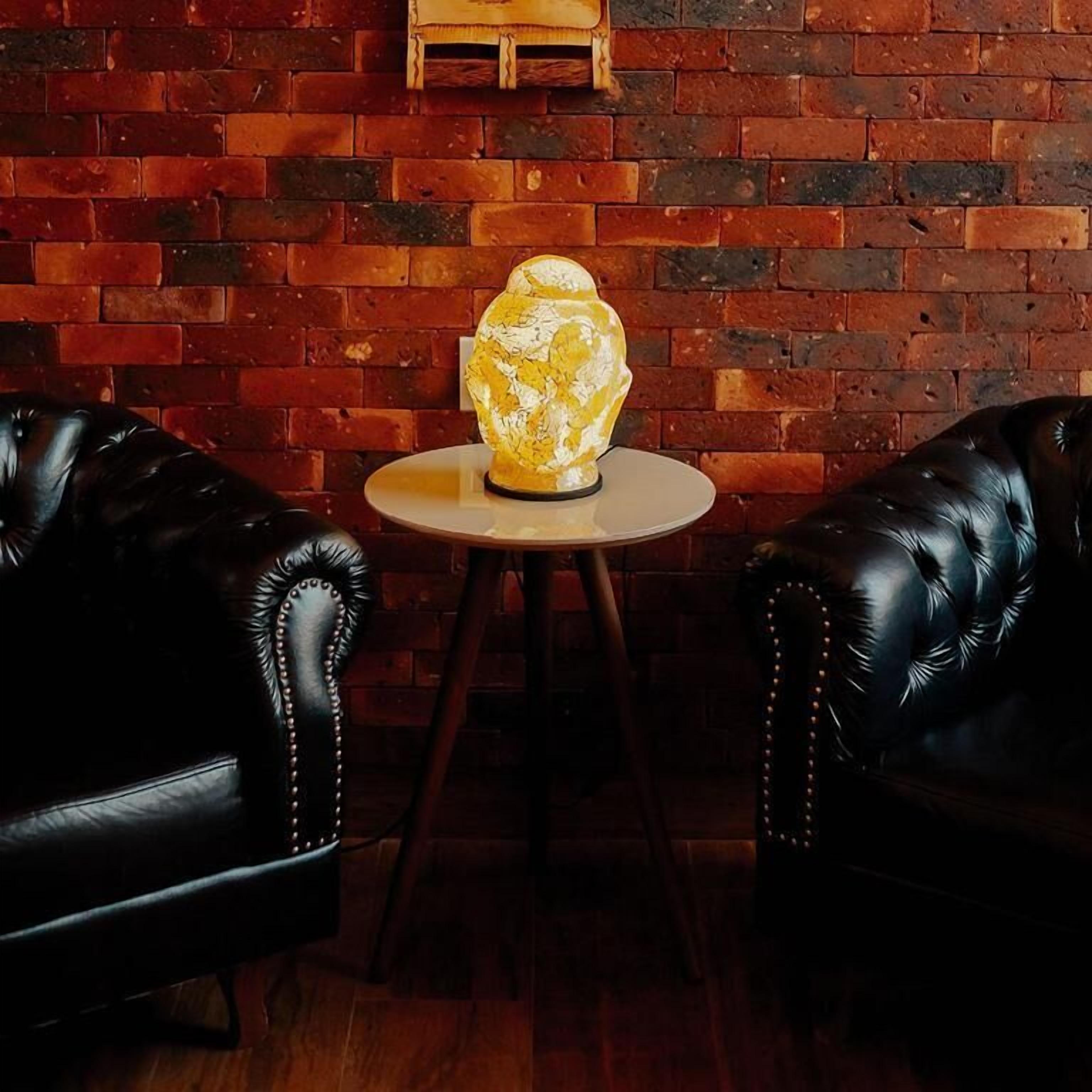 Una habitación con pared de ladrillo, dos sillones de cuero negro y una mesa redonda con un objeto decorativo.