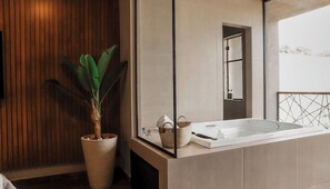 A modern bathroom with a wooden panel wall, a large potted plant, a bathtub, and a mirror reflecting a snowy outdoor view. - Pousada Quinta dos Cabeças (Capitólio)