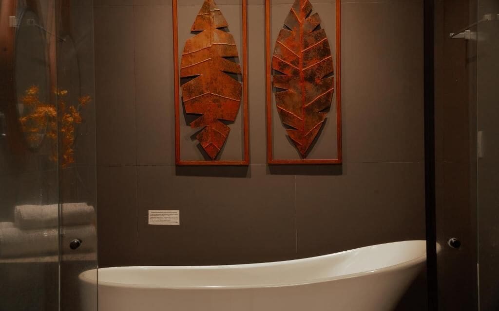Casa de banho com uma banheira branca, duas obras de arte decorativas com folhas e um box de chuveiro em vidro.