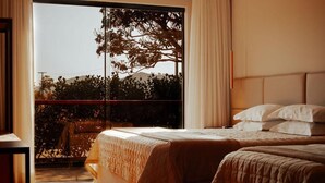 Un dormitorio con un ventanal grande, una cama con cabecera y vistas a árboles y colinas.