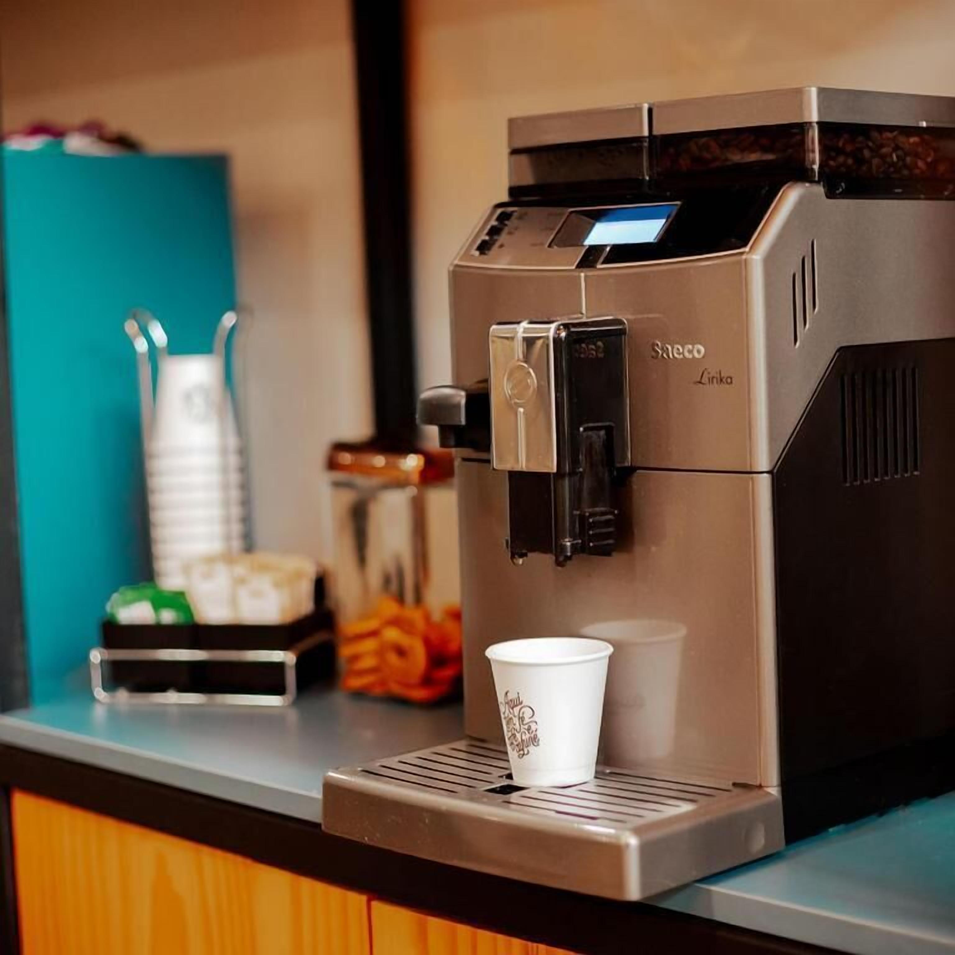Máquina de café moderna com visor digital, uma xícara de café e um pequeno recipiente de leite condensado em uma bancada.