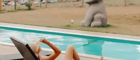 A person relaxing on a lounge chair by a pool with a large statue in the background.
