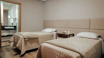 A hotel room with two beds, a bedside table, a mirror, and a bathroom visible through a glass door.